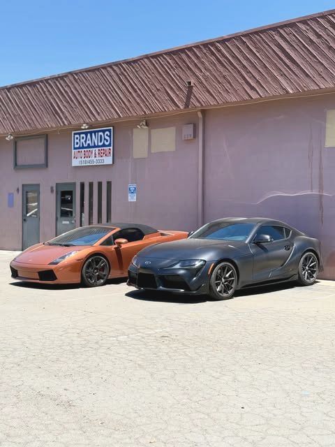 A Lamborghini Gallardo and a Toyota Supra parked outside the Brands Auto Body shopfront